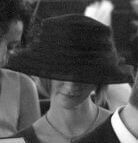 A person wearing a wide-brimmed black hat, facing downwards, with a necklace visible.