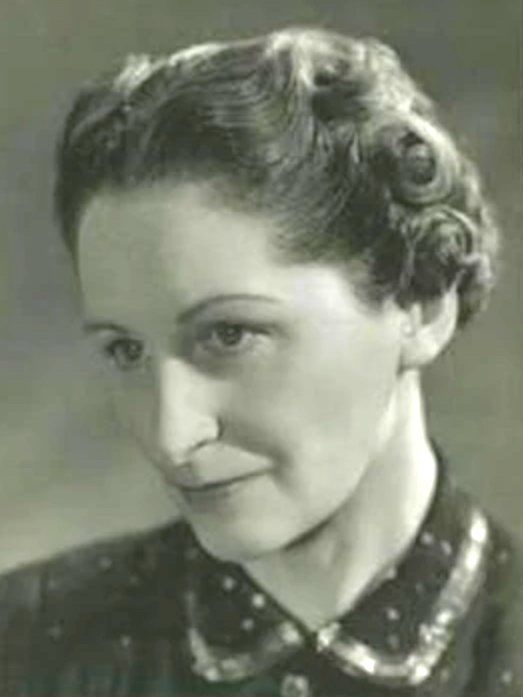 A monochromatic portrait of a person with curled hair, wearing a patterned collared shirt, looking slightly away.