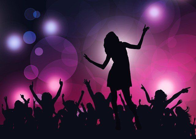 Silhouetted figures dance at a party with raised arms against a purple and pink bokeh light background.