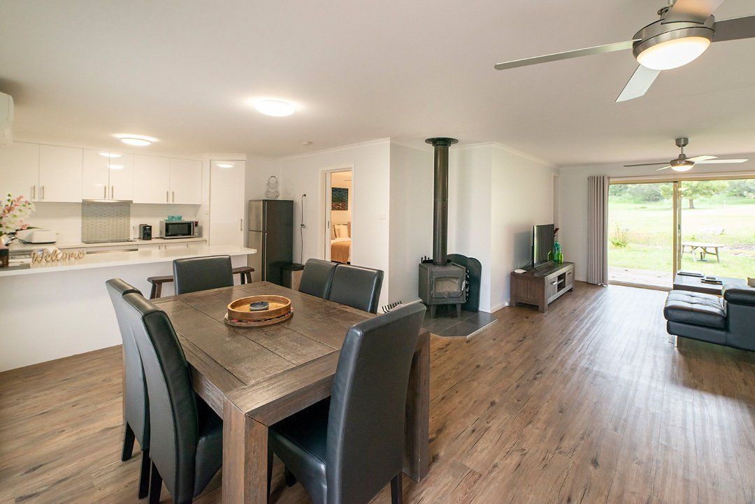 Open plan kitchen and dining area adjoining living area with large smart TV at Hideaway Villa, Halls Gap Valley Lodges.