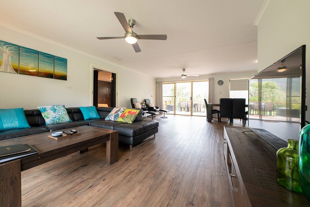 Open plan kitchen and dining area adjoining living area with large smart TV at Hideaway Villa, Halls Gap Valley Lodges.