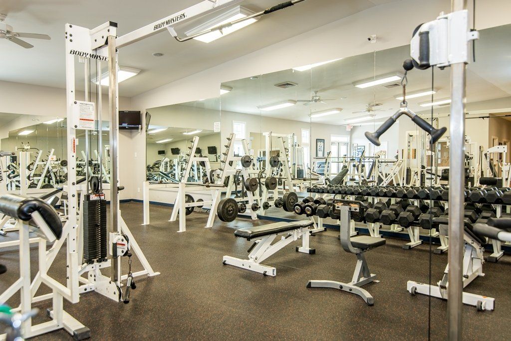 A large gym filled with lots of exercise equipment and dumbbells.