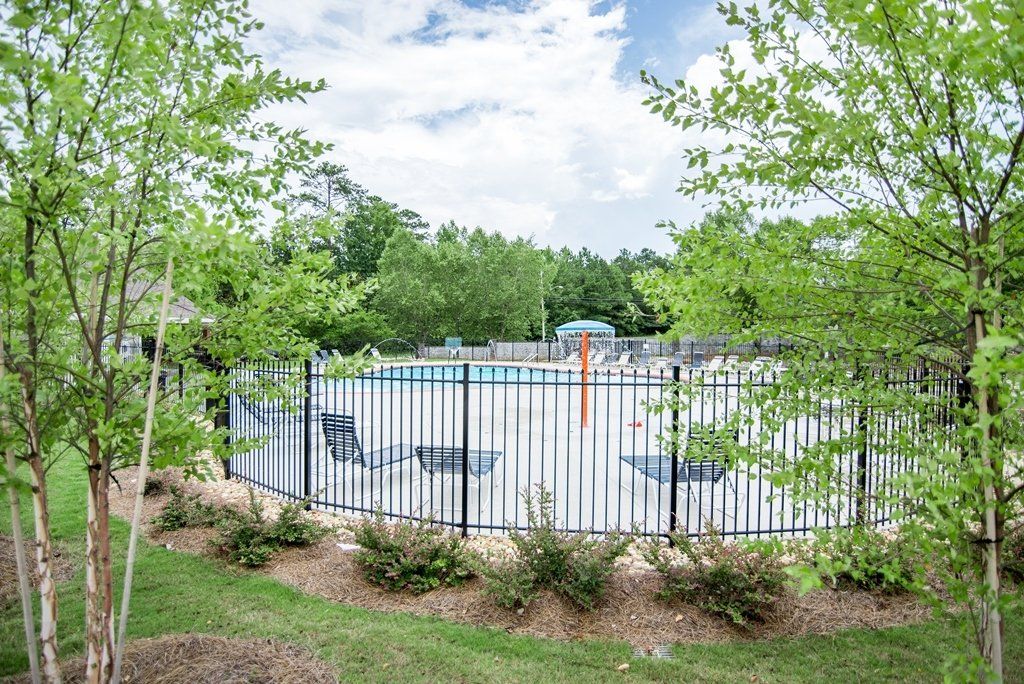 A fence surrounds a swimming pool surrounded by trees and grass.