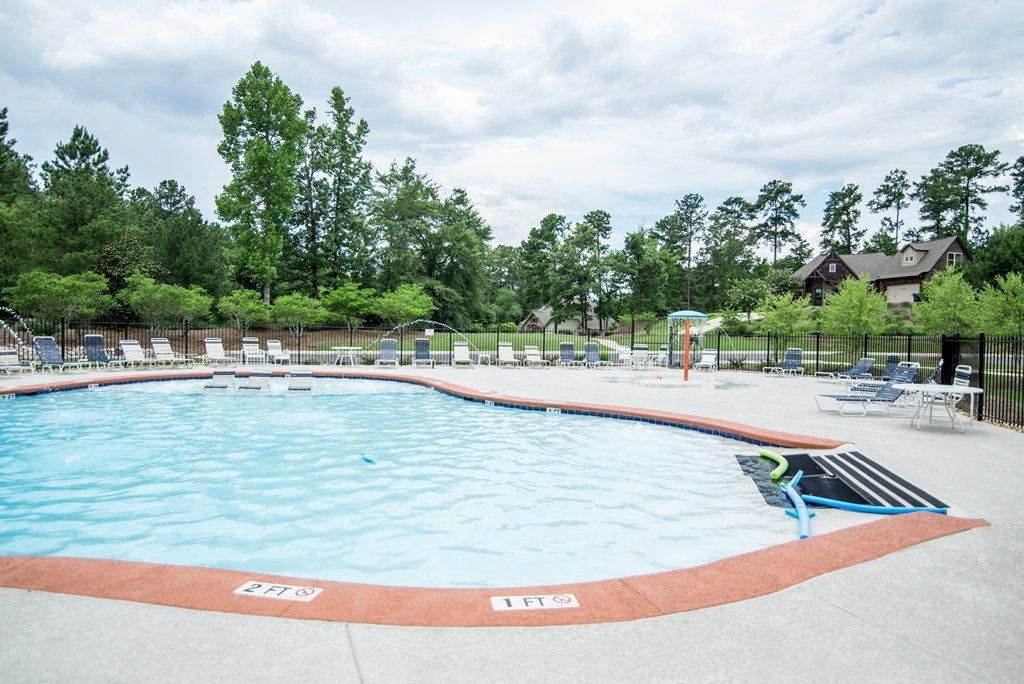 A large swimming pool surrounded by chairs and trees on a cloudy day.