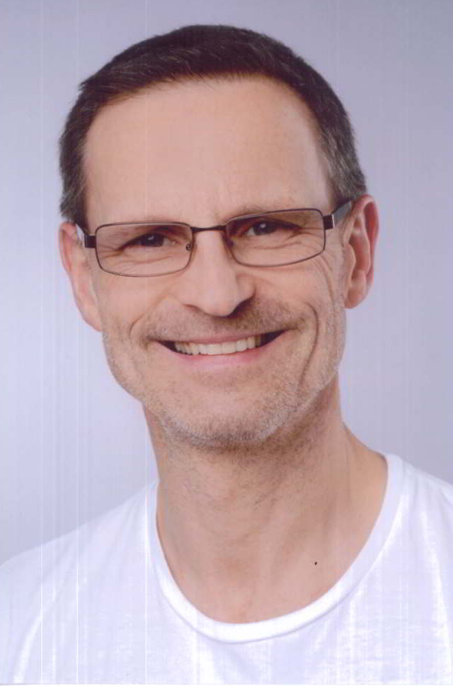 Ein Mann mit Brille und weißem Hemd lächelt in die Kamera.