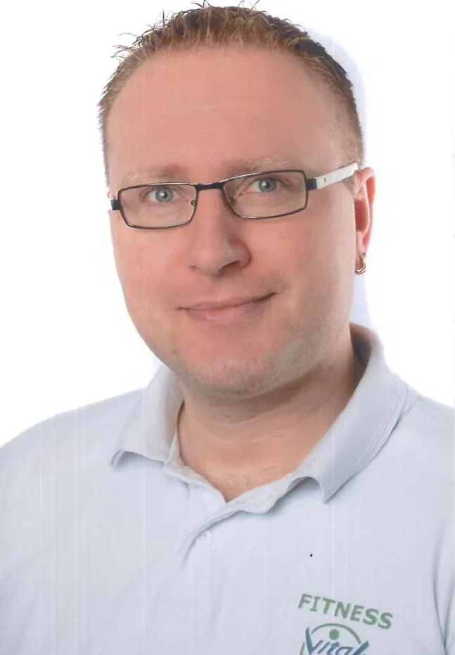 Ein Mann mit Brille und weißem Shirt mit der Aufschrift „Fitness“