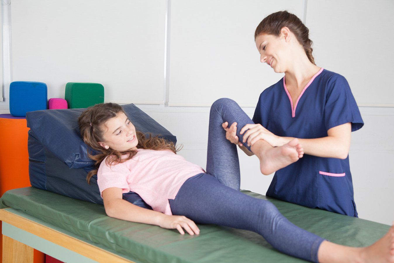 Eine Krankenschwester hilft einem jungen Mädchen, ihr Bein auf einem Bett auszustrecken.