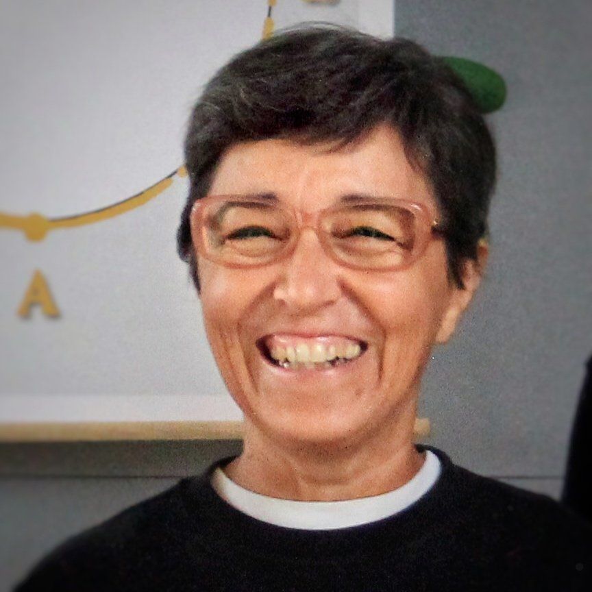 Una donna con gli occhiali e un maglione nero sorride.