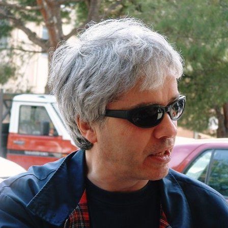 Un uomo che indossa occhiali da sole e una camicia a quadri guarda la telecamera