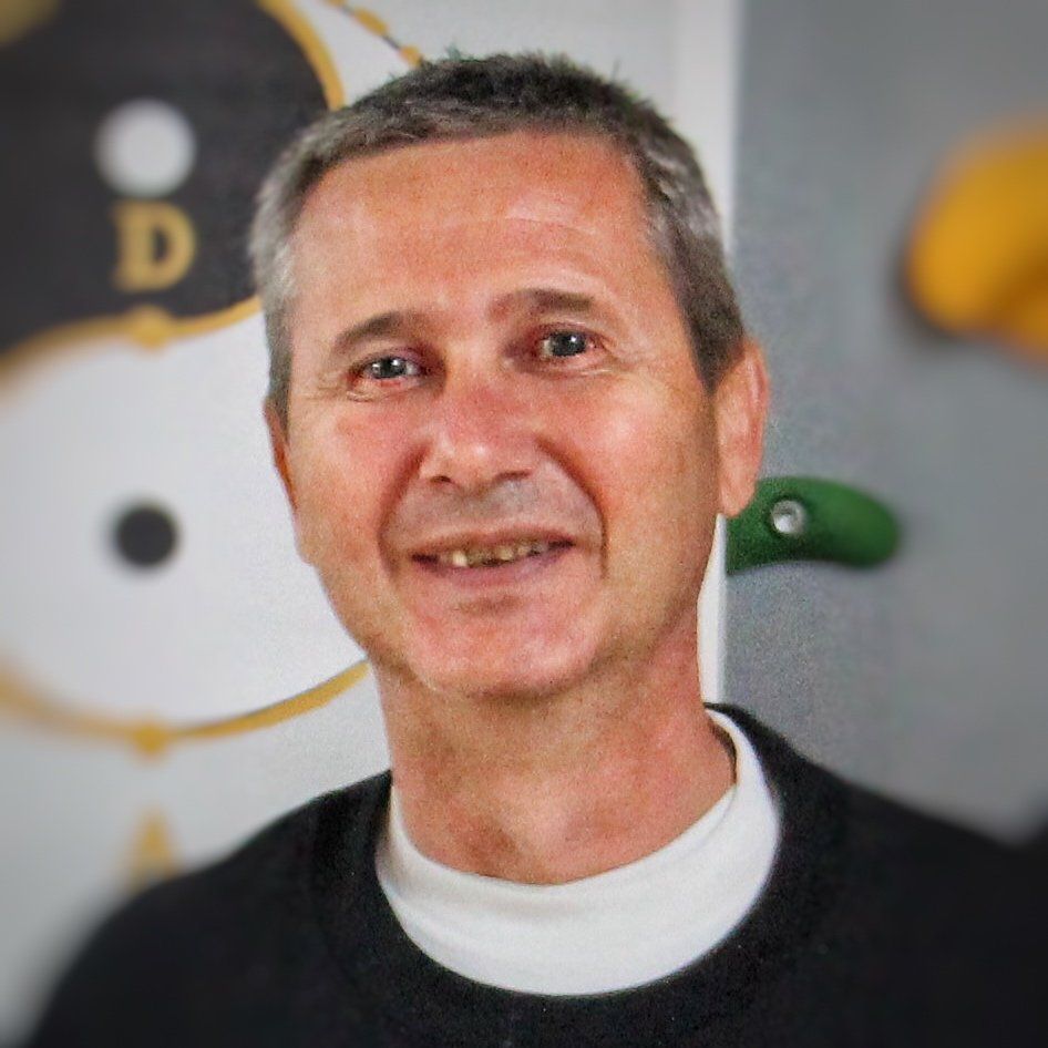 Un uomo che indossa un maglione nero e una camicia bianca sorride alla telecamera.