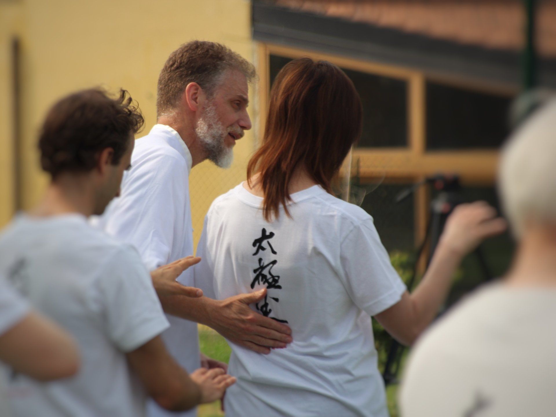 Un uomo con la barba parla con una donna che indossa una camicia bianca con scritte cinesi sulla schiena