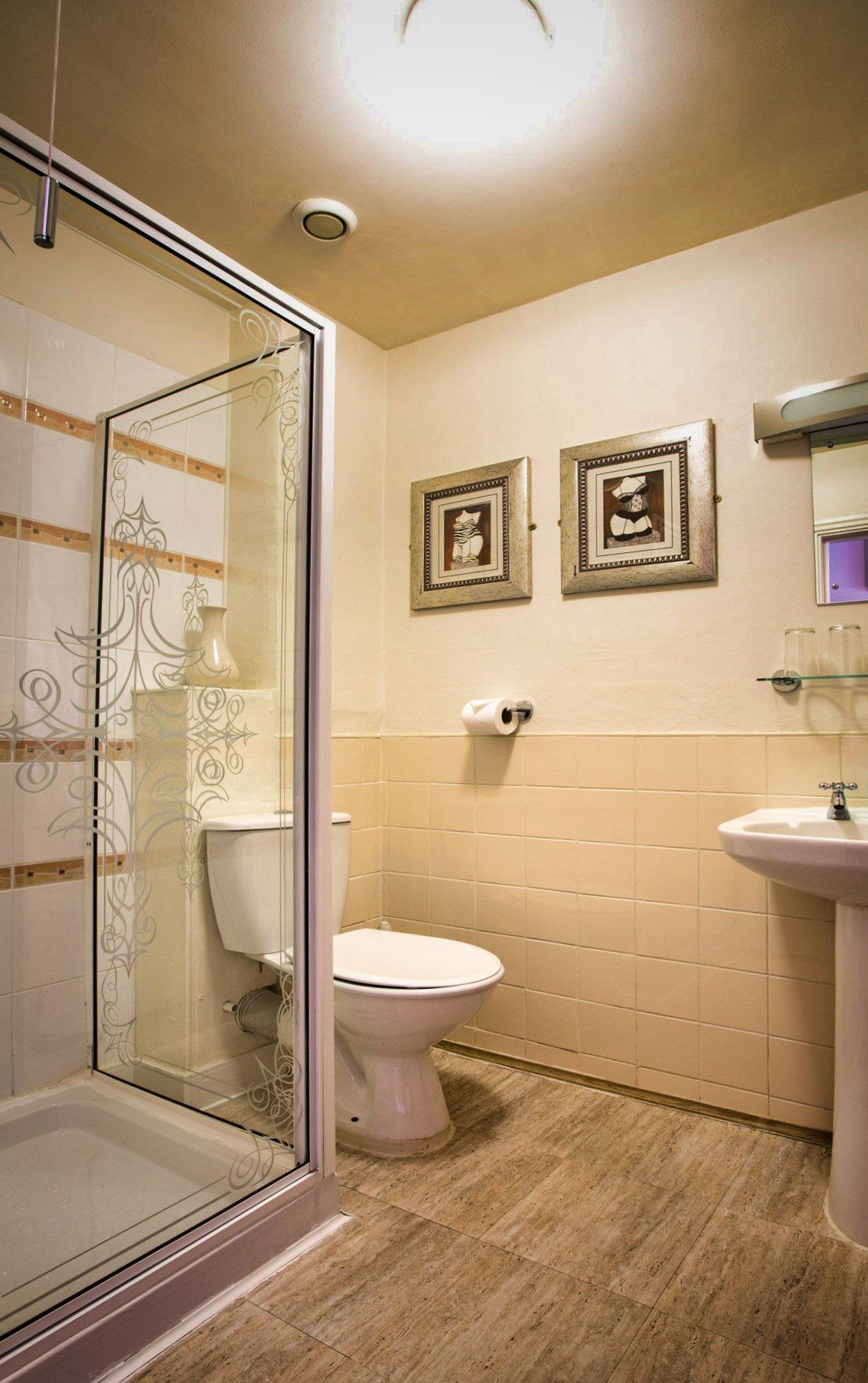 Bathroom with shower, toilet, and sink. Beige walls, wood-look floor, framed pictures above the toilet.