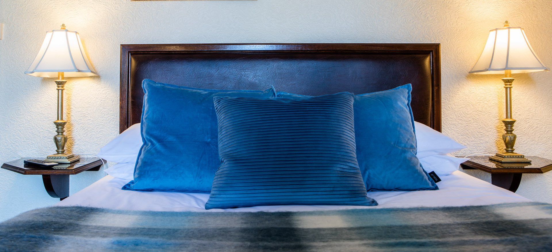 Bedroom with blue pillows, two lamps on nightstands, and a patterned blanket.