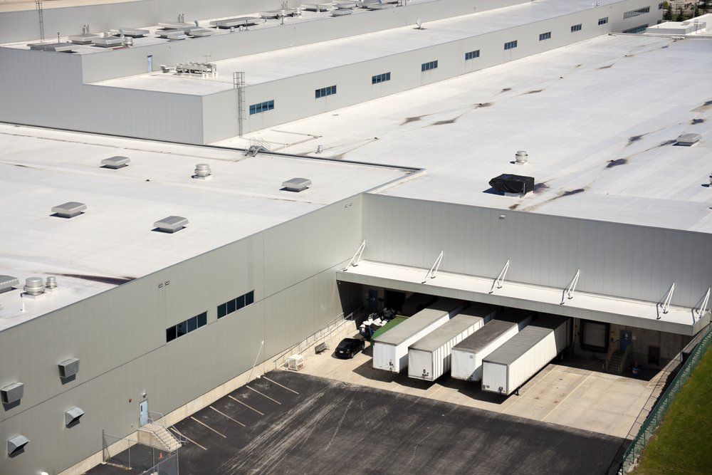 Aerial view of a large white warehouse with loading docks and several trucks parked outside.