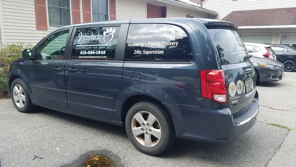 Dark blue minivan parked on a driveway with business logos on the windows.