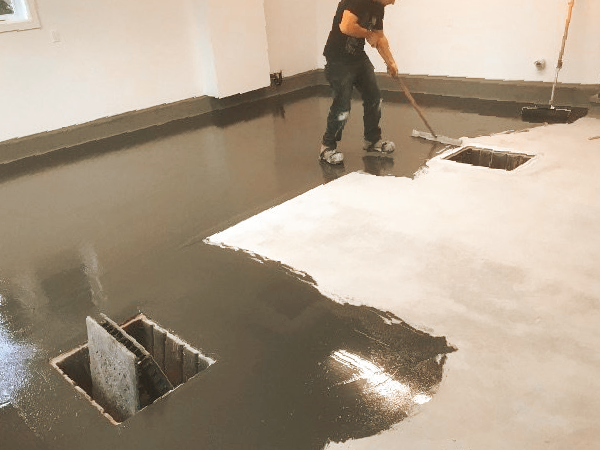 Person applying gray epoxy floor coating in a room, partially finished.