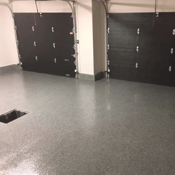 Sol de garage recouvert d'époxy avec deux portes de garage noires fermées, sol gris avec un drain encastré.