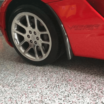 Red sports car wheel and body, on a multi-colored speckled garage floor.