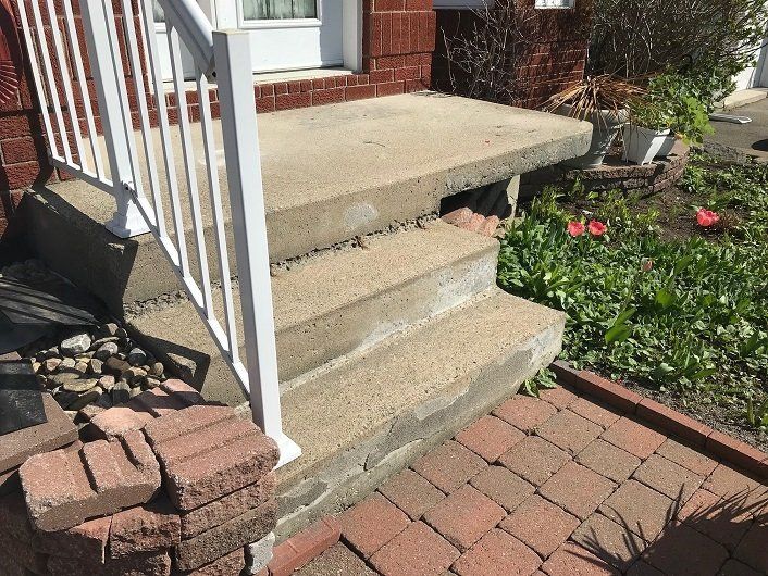 Concrete steps and landing with white railing, brick facade, and landscaping.