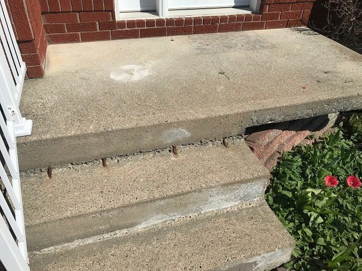 Concrete front porch with steps and brick wall. White railing on the left.
