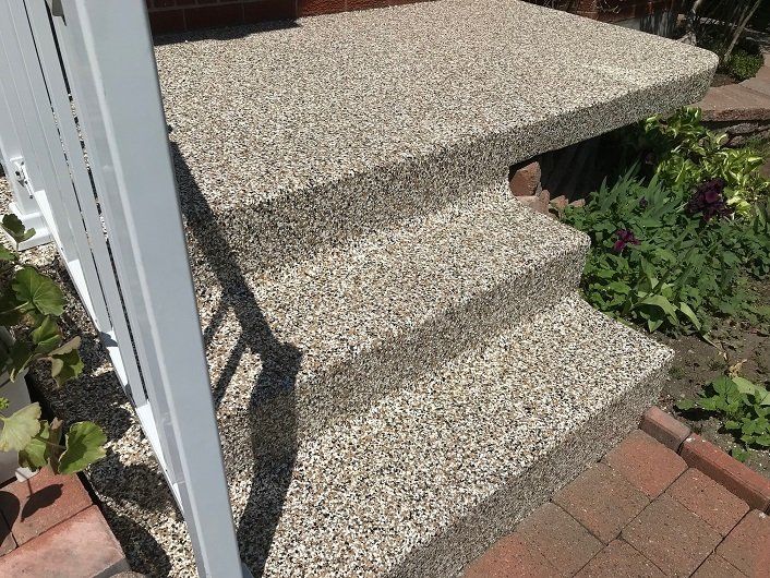 Concrete steps and porch with a textured, pebble-like finish. White railing on the left, brickwork on the right.