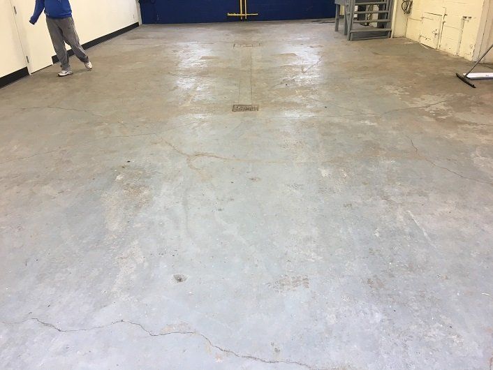 Person walking on a gray concrete floor, in a room with a blue wall and a metal table.