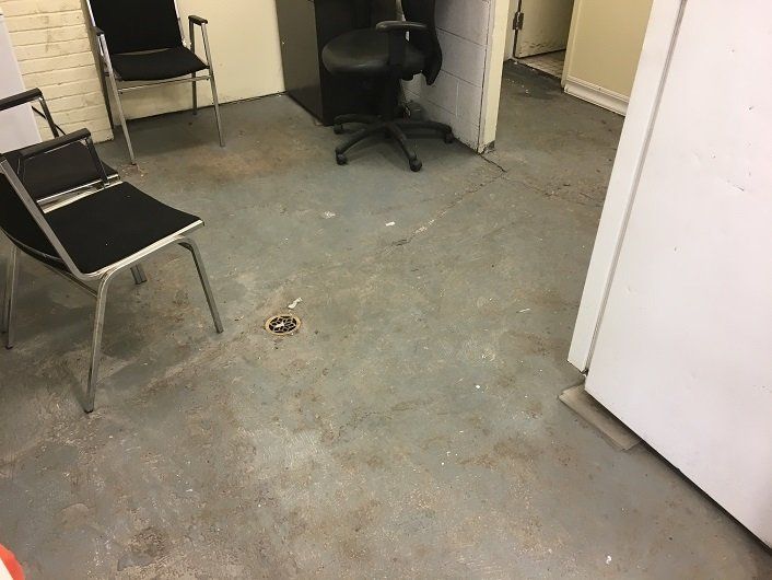 Concrete floor with stains, two chairs, a desk chair, and a white door.