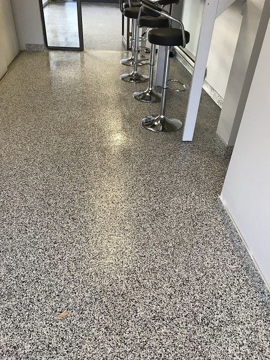Gray speckled epoxy flooring with bar stools alongside a white wall.