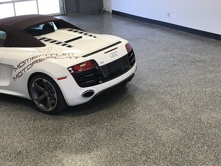 White Audi R8 convertible in a garage with a speckled gray floor.