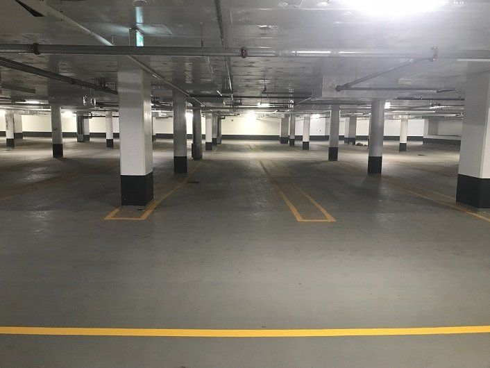 Empty, indoor parking garage with gray floor, white support pillars, and yellow parking lines.