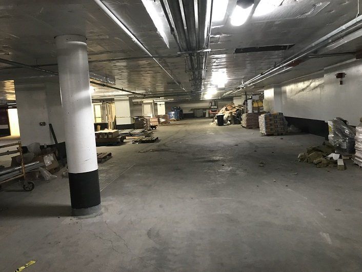 Underground parking area with concrete floor, pillars, and various construction materials scattered about.