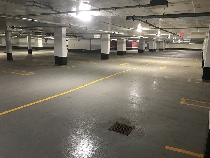 Empty underground parking garage with gray floor and white pillars. Yellow lines mark the roadway.