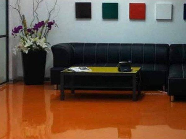 Orange glossy floor in a room with black leather couch, black coffee table, colorful squares on white wall, and flower arrangement.