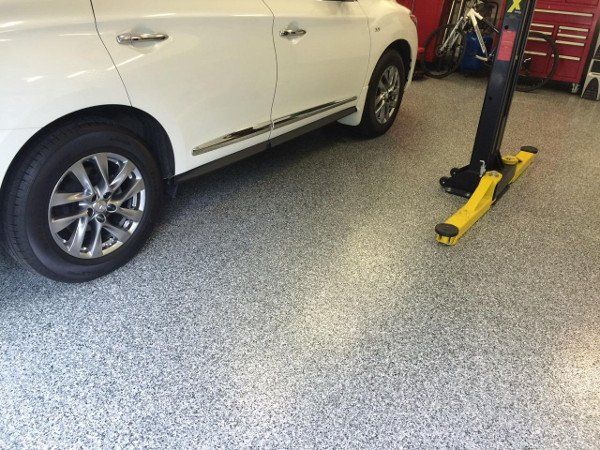 White SUV parked on a speckled gray garage floor next to a yellow lift.