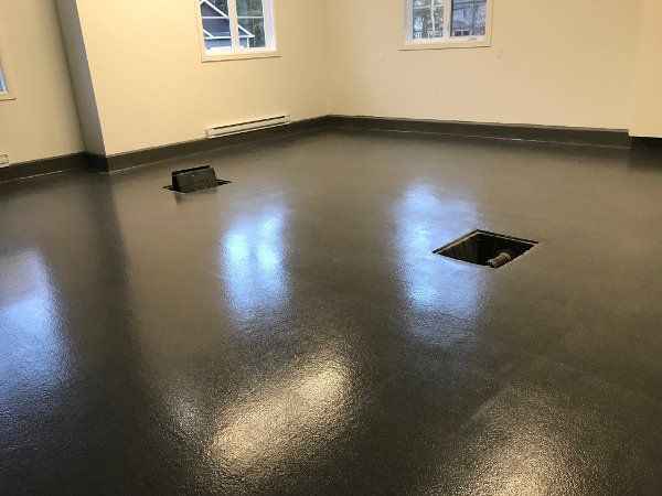 Empty room with shiny, dark gray epoxy floor, windows, and two square openings.