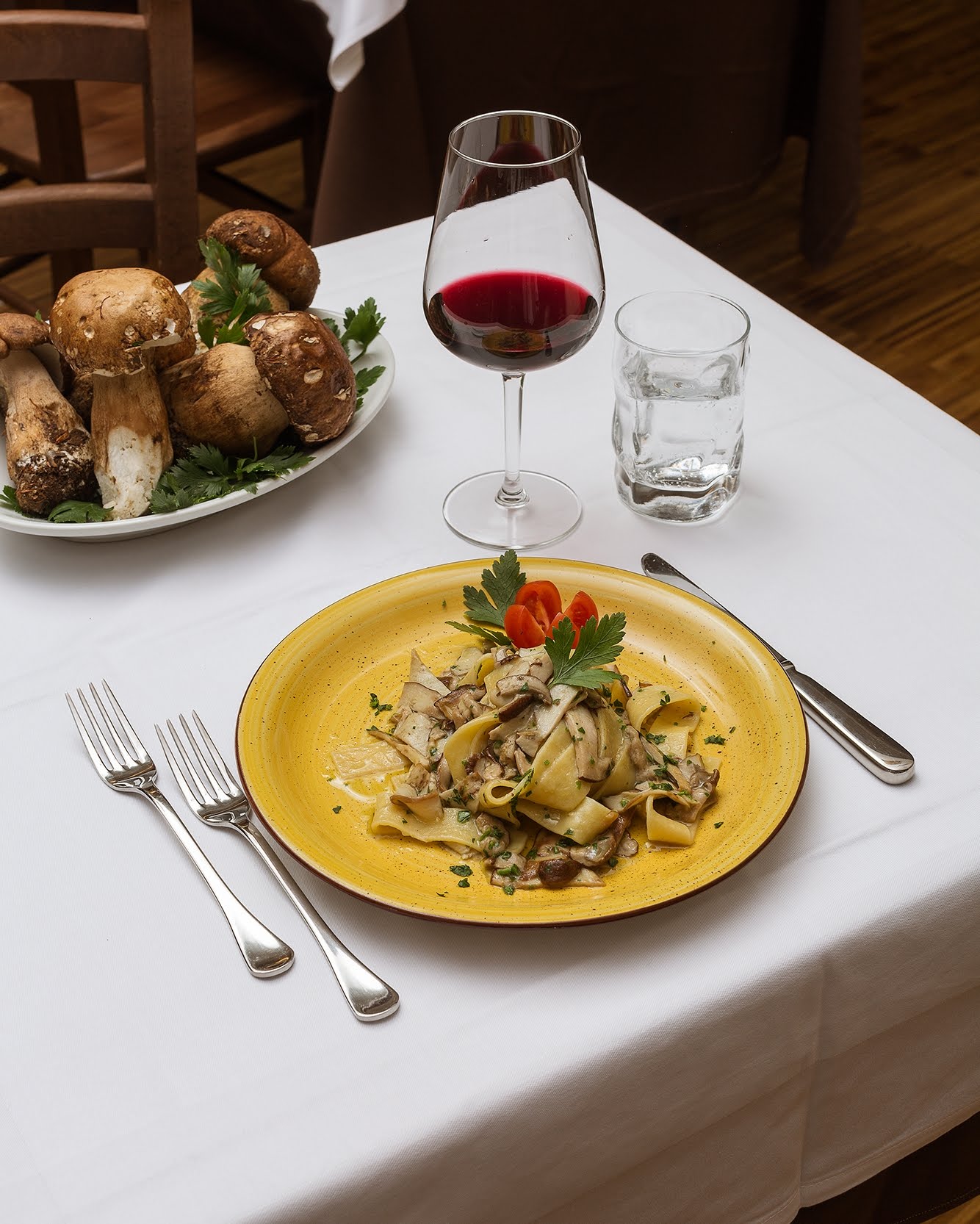 Pasta con funghi e vino su un tavolo apparecchiato con posate e un piatto di funghi.