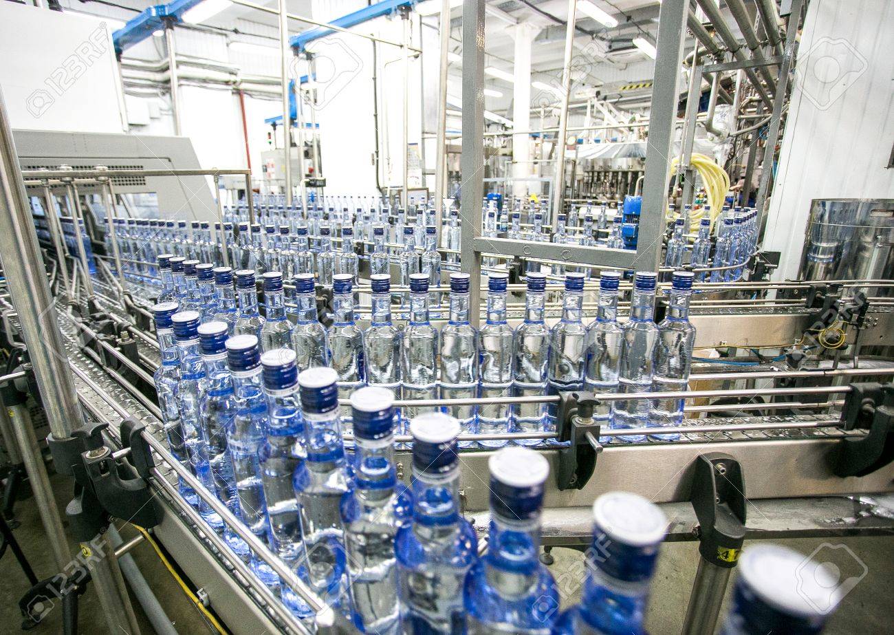 Botellas de agua con tapón azul moviéndose en una línea de embotellado en una fábrica luminosa.