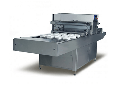 Máquina industrial de corte de papel de color gris con mesa de alimentación plana y componentes traseros apilados.