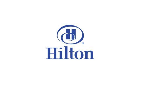 Logotipo de Hilton en texto azul con emblema circular sobre fondo blanco.