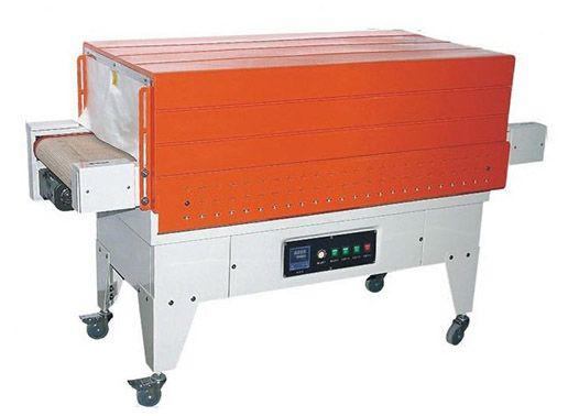 Máquina industrial de retractilado de color naranja con cinta transportadora sobre soporte metálico y panel de control.