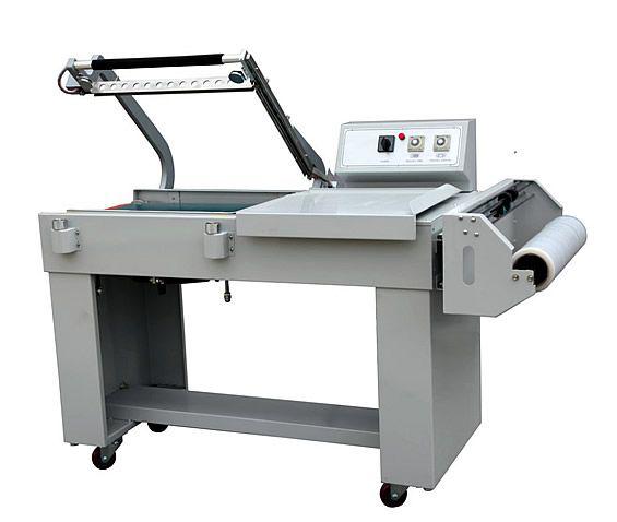 Máquina de prensado térmico industrial con carcasa gris, panel de control y rollo de material a la derecha.
