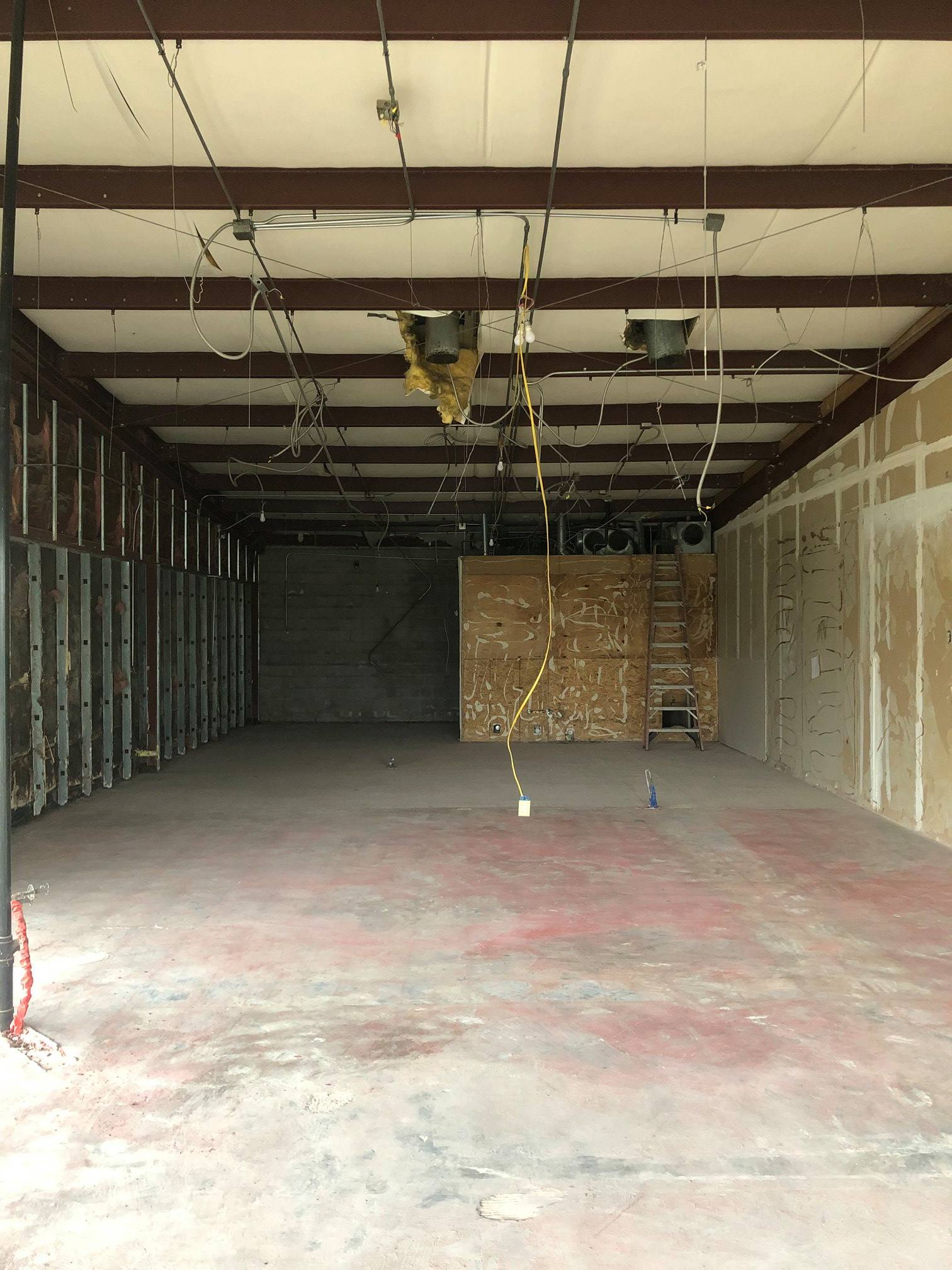 Empty unfinished garage interior with exposed ceiling beams, concrete floor, and plywood wall paneling