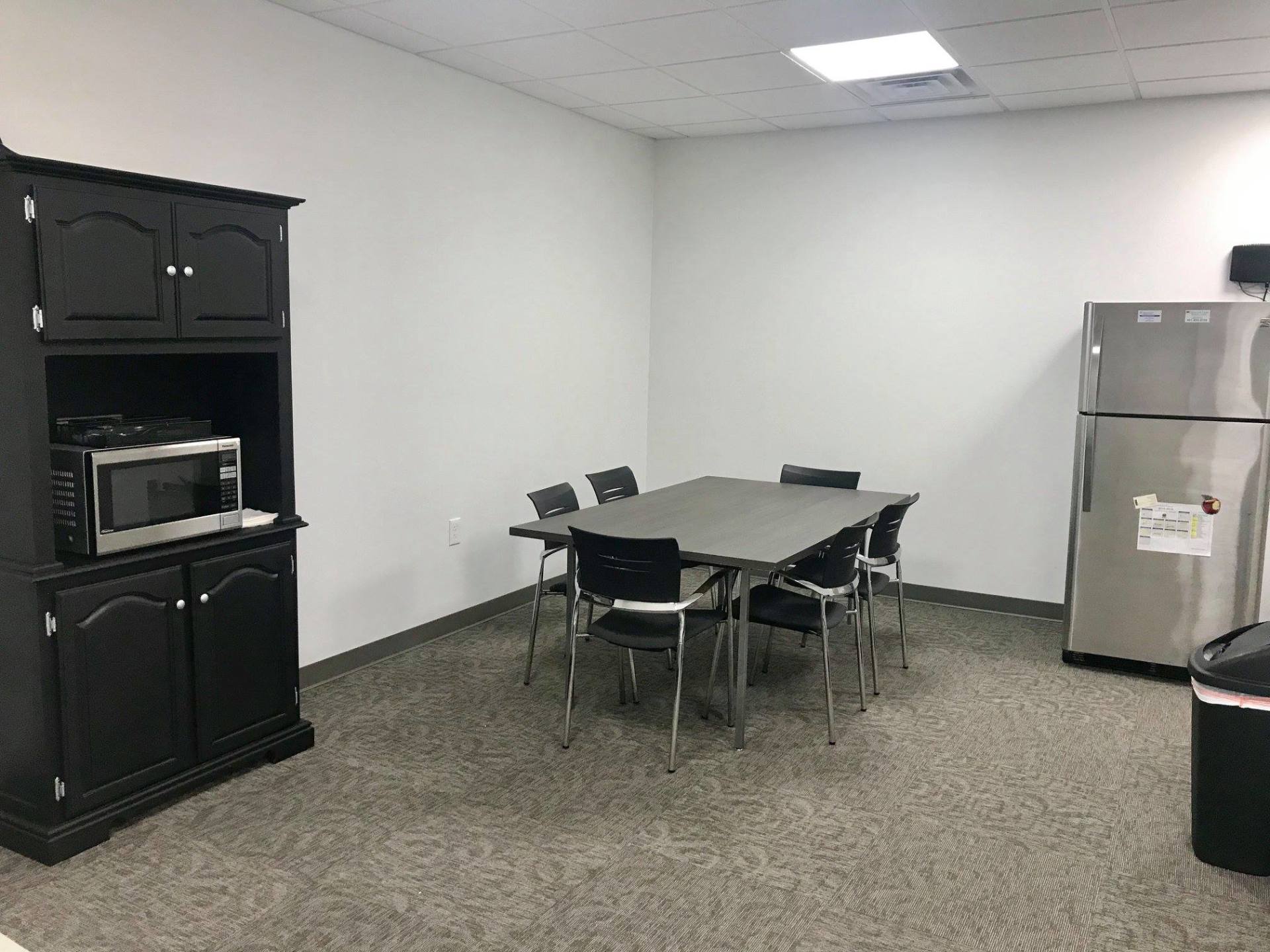 Small break room with table and chairs, black cabinet, microwave, and stainless steel refrigerator.