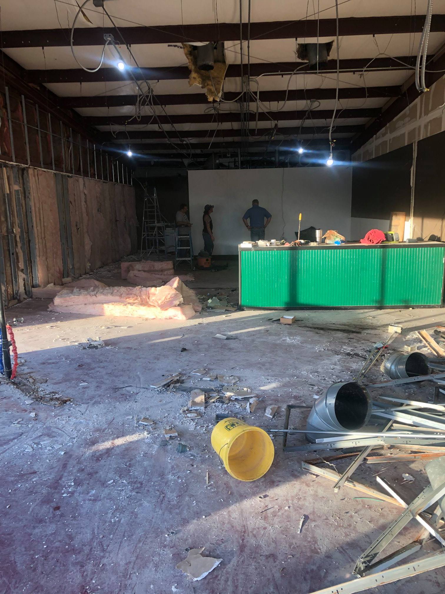 Damaged room with debris on the floor, a green table, and exposed ceiling beams