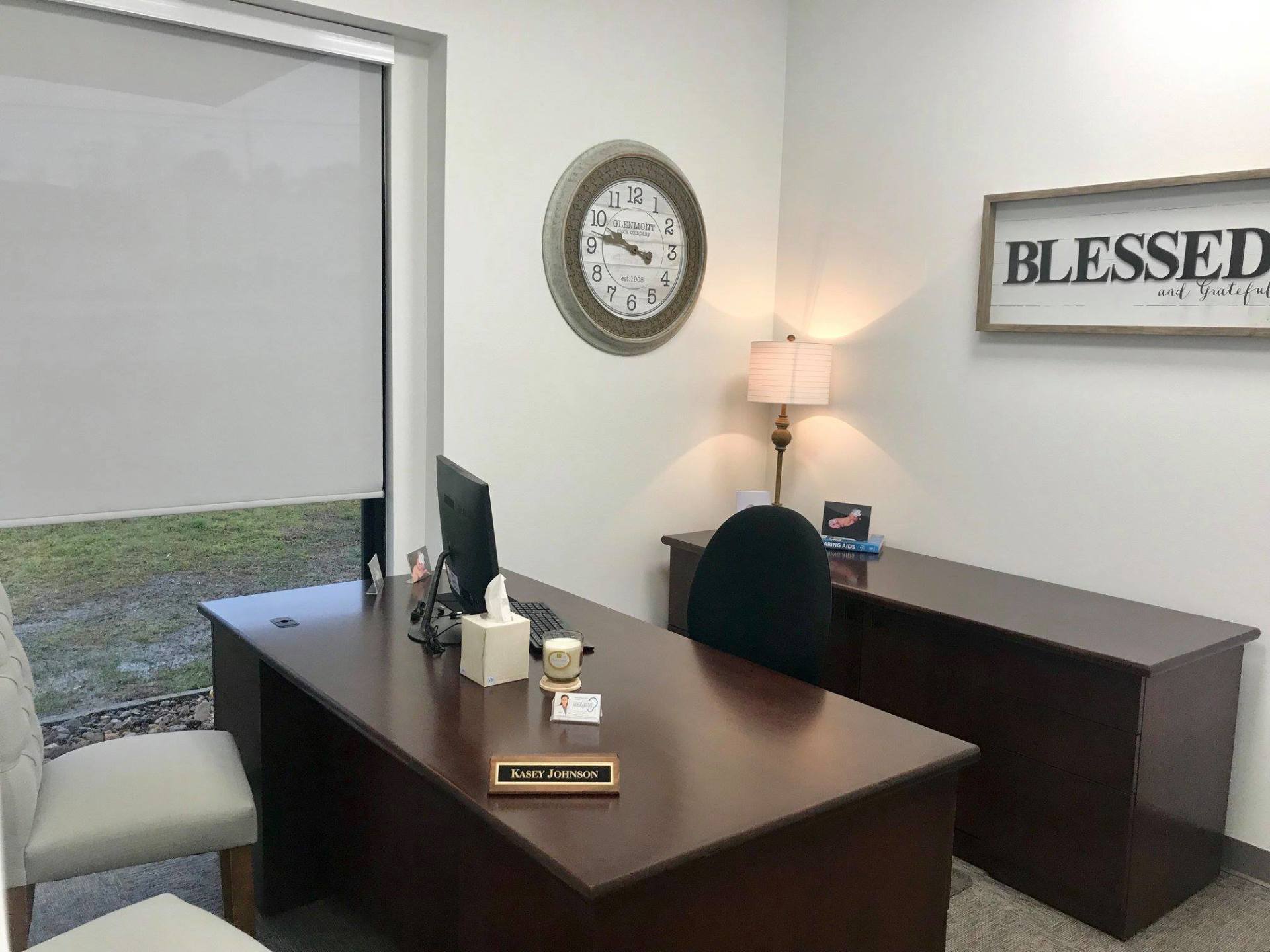 Empty office with dark wood desk, chair, lamp, clock, and “BLESSED” wall sign.