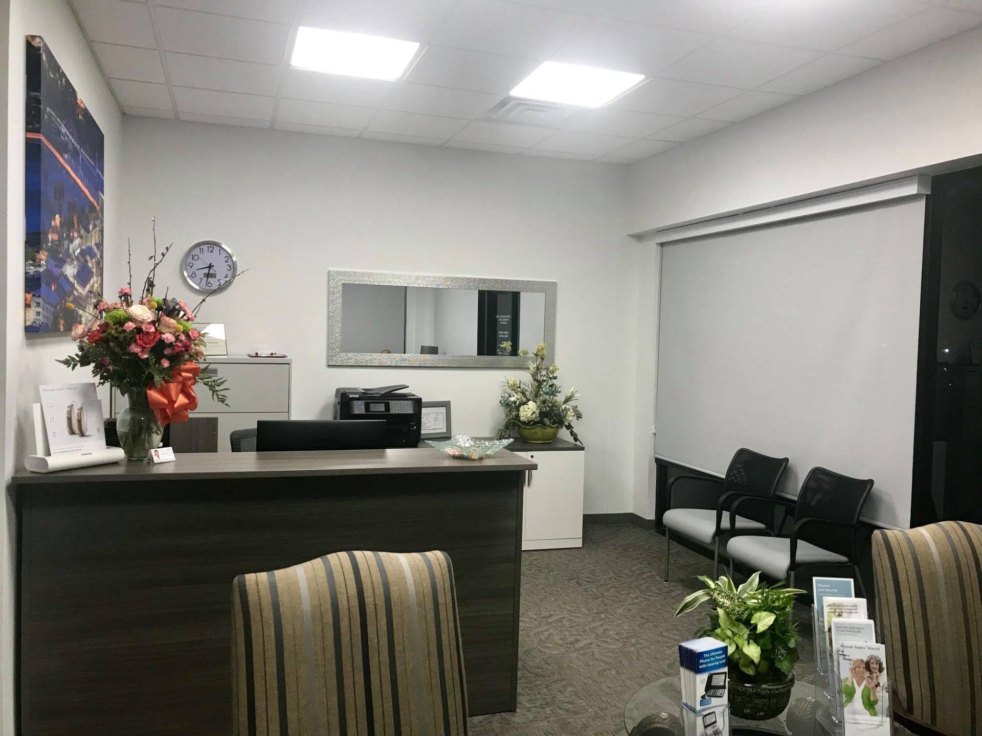 Empty office reception area with desk, chairs, flowers, and a closed window blind