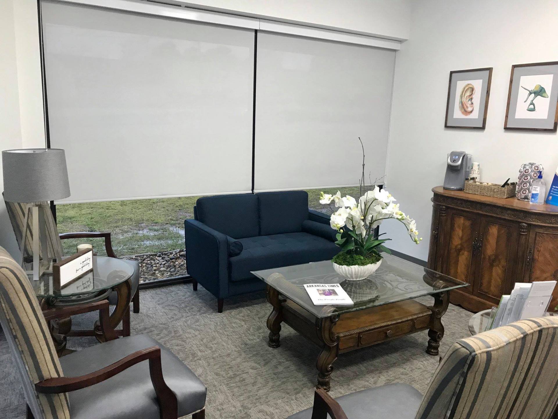 Living room with blue sofa, glass coffee table, lamp, and wooden cabinet by a window with closed blinds