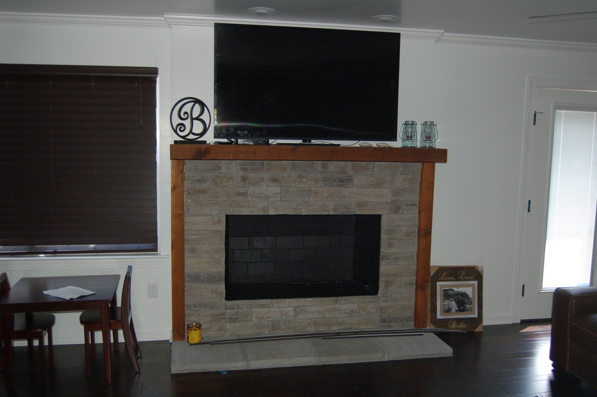 Living room fireplace with mounted TV, stone surround, and dark blinds at left and right