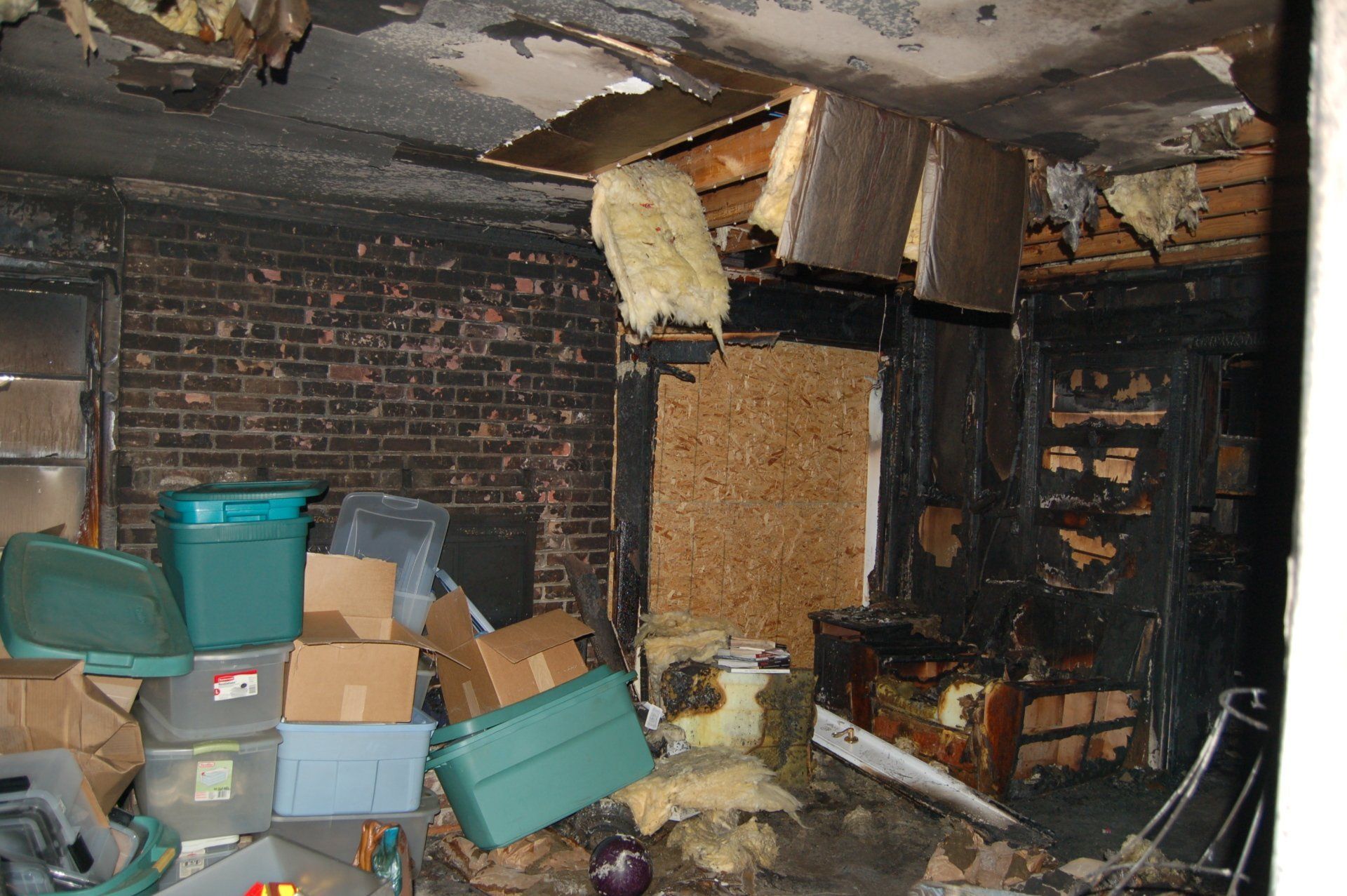 Damaged room with collapsed ceiling, brick walls, and stacked storage bins and boxes in a cluttered corner