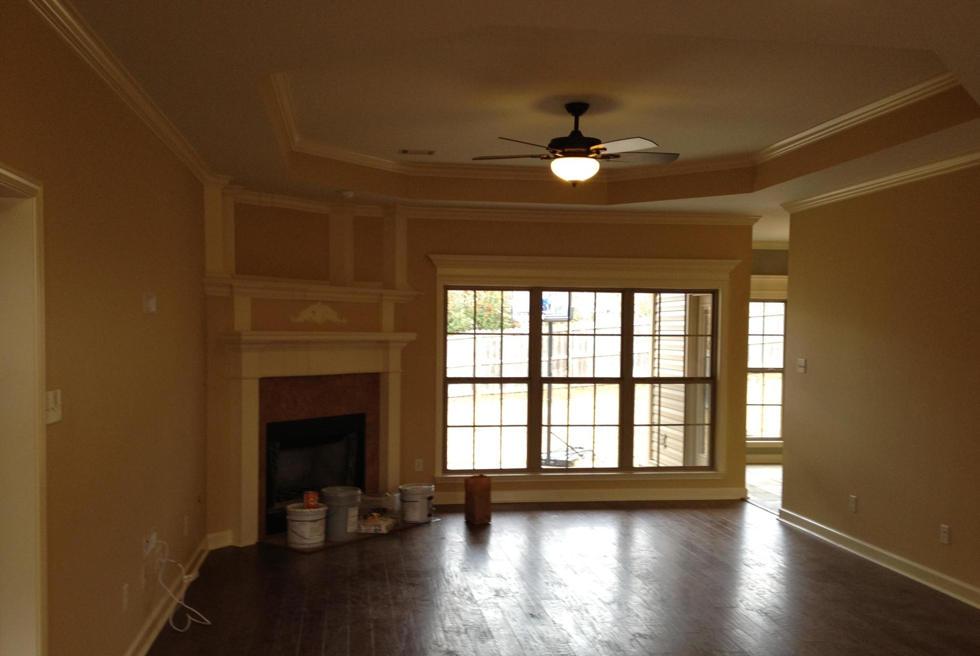 Empty living room with fireplace, ceiling fan, and large windows letting in daylight